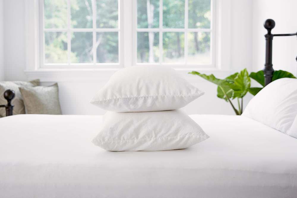 Stack of two white pillows on top of a white comforter.