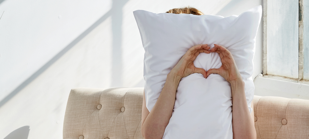 Girl behind pillow with hands in a heart-shape