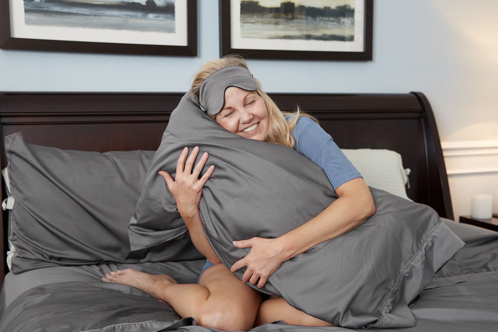 Nollapelli founder & CEO Allison Howard hugging charcoal gray cooling bedding made for menopausal women experiencing hot flashes and night sweats.